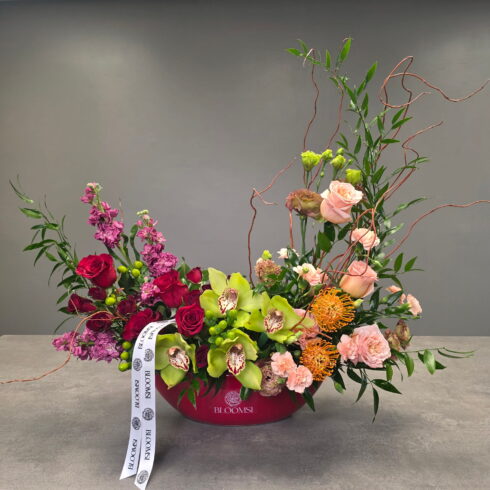 Luxury floral arrangement with green orchids, red and blush roses, and sculptural greenery in a designer pot in Toronto and GTA.