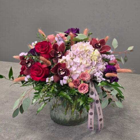 Luxury plum and rouge floral design with roses, orchids and hydrangea arranged in a glass vase by BLOOMSI
