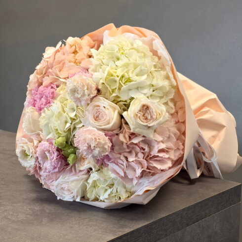 Luxury blush hydrangea bouquet with cream roses and ranunculus wrapped in soft pink paper by BLOOMSI