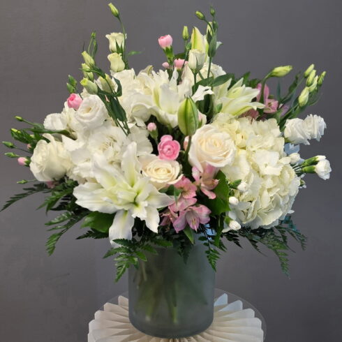 Elegant white and blush flower arrangement with lilies, roses and hydrangea in a glass vase by BLOOMSI Toronto